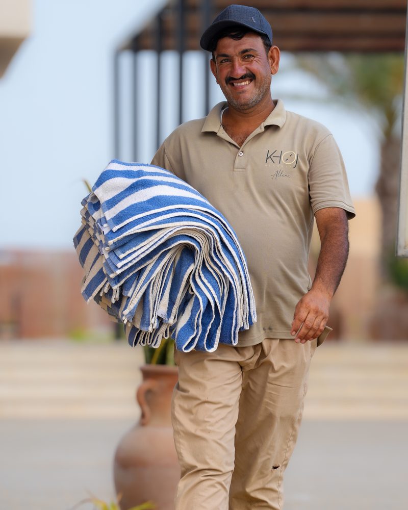 Resort worker smiling while carrying a stack of striped towels