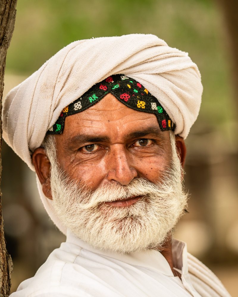 Elderly man in a white turban with an embroidered band, smiling at the camera